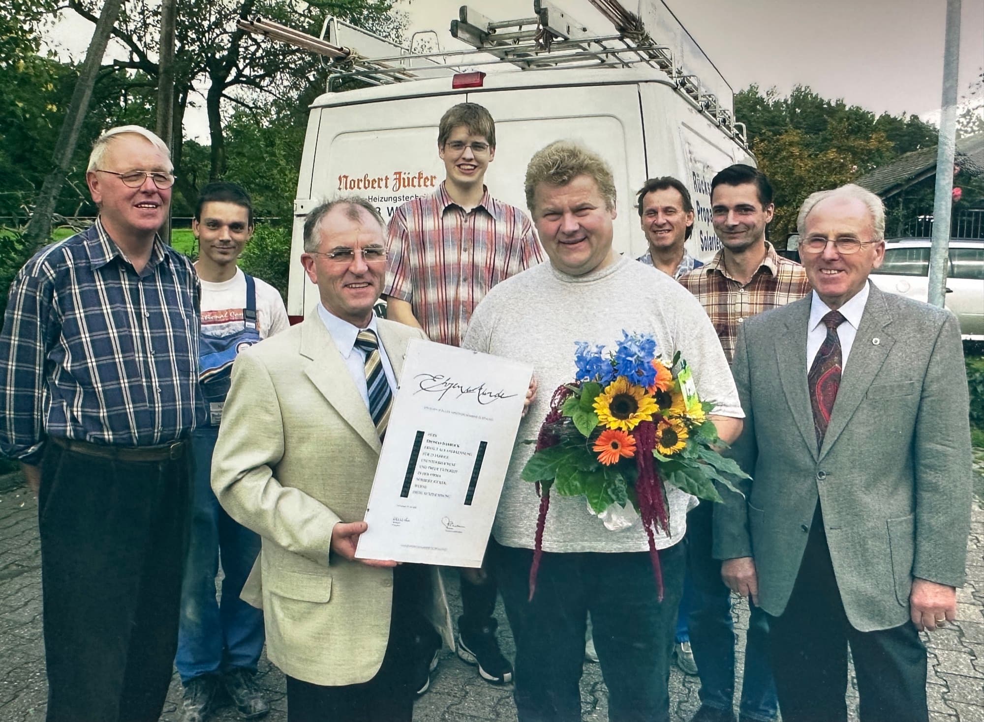 Das Team von Sanitär Jücker mit der Ehrenurkunde für Thomas Dabrock, vor dem Firmenwagen von Norbert Jücker